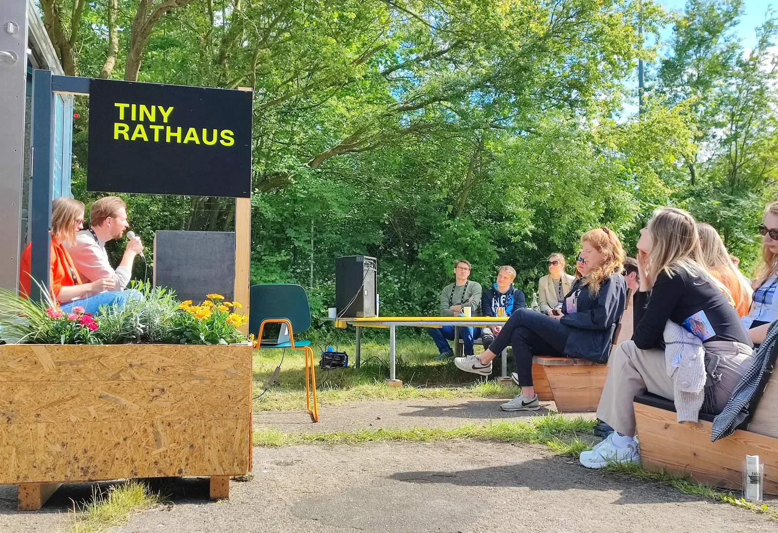 Menschen im Gespräch im Freien unter einem Schild 'Tiny Rathaus'
